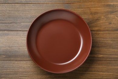 Empty brown ceramic plate on wooden table, top view