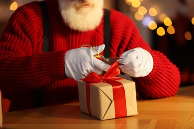 Photo of Santa Claus tying bow on gift box at his workplace in room decorated for Christmas, closeup