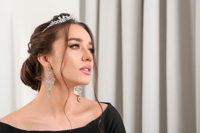 Beautiful young woman wearing luxurious tiara indoors, space for text