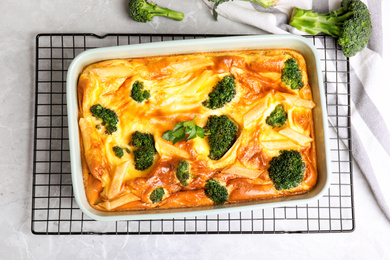 Photo of Tasty broccoli casserole in baking dish on cooling rack, flat lay