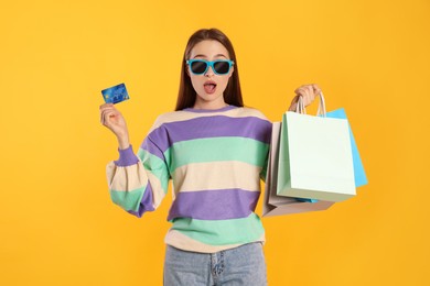 Photo of Surprised young woman with shopping bags and credit card on yellow background. Big sale