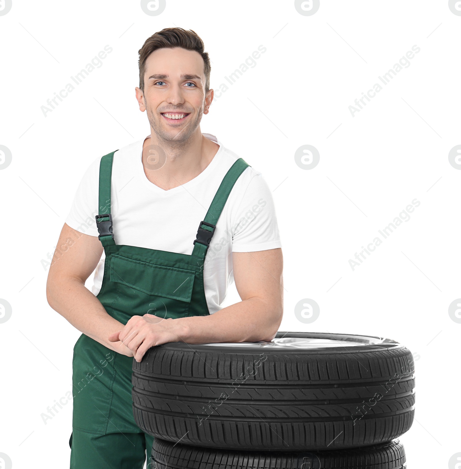 Photo of Young mechanic in uniform with car tires on white background