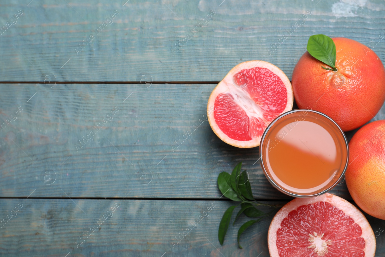 Photo of Tasty freshly made grapefruit juice and fruits on blue wooden table, flat lay. Space for text