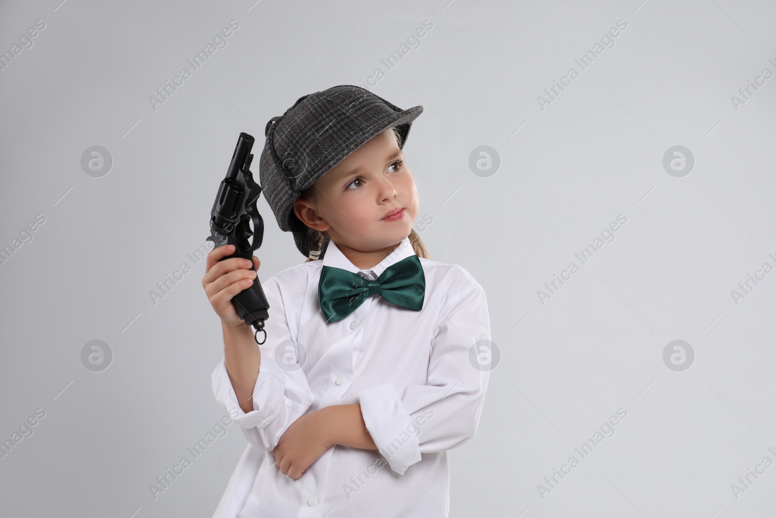 Photo of Cute little detective with revolver on grey background