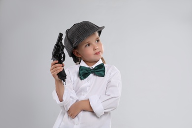 Photo of Cute little detective with revolver on grey background