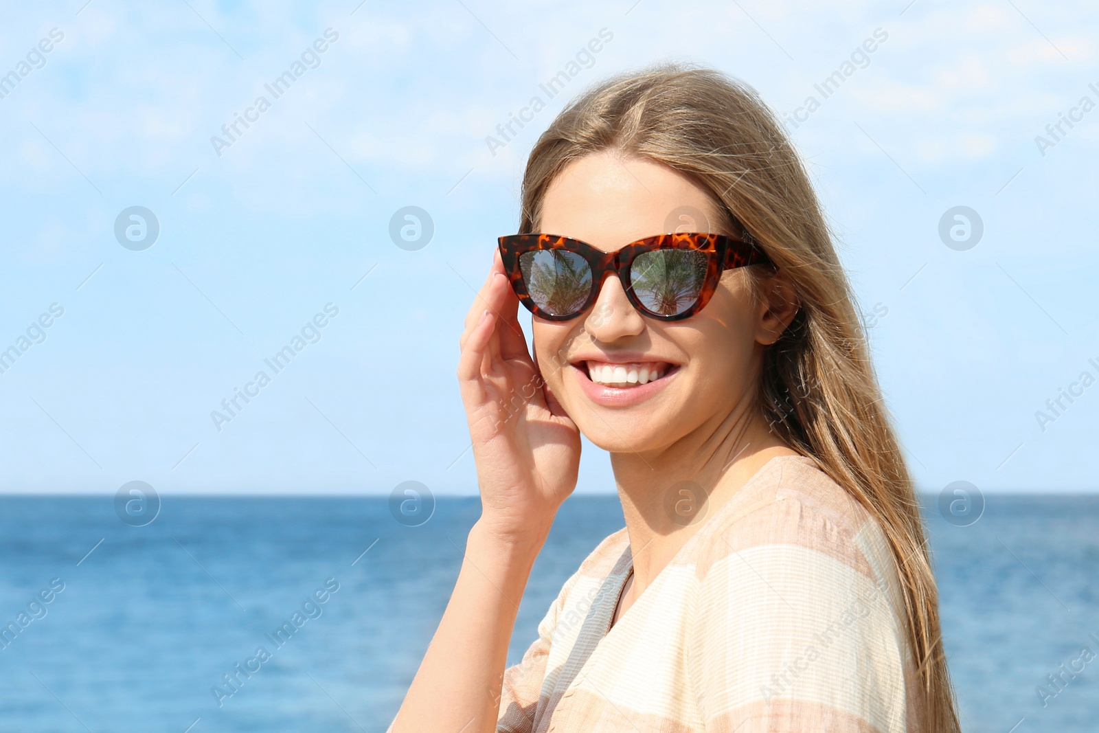 Image of Young woman wearing stylish sunglasses with reflection of palm trees near sea 