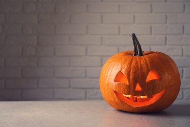 Photo of Halloween pumpkin head jack lantern on table against brick wall with space for text