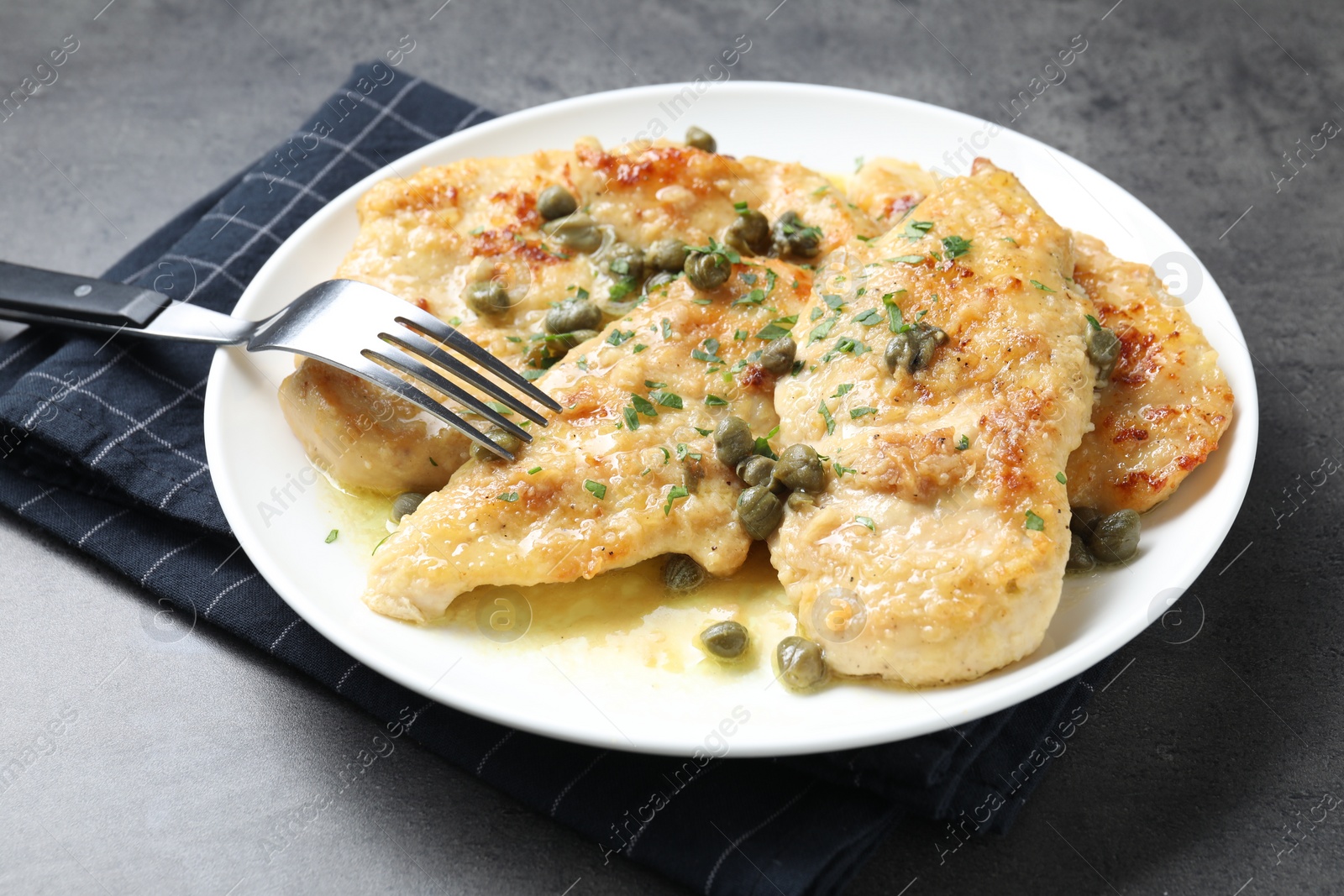 Photo of Delicious chicken piccata with herbs served on grey table