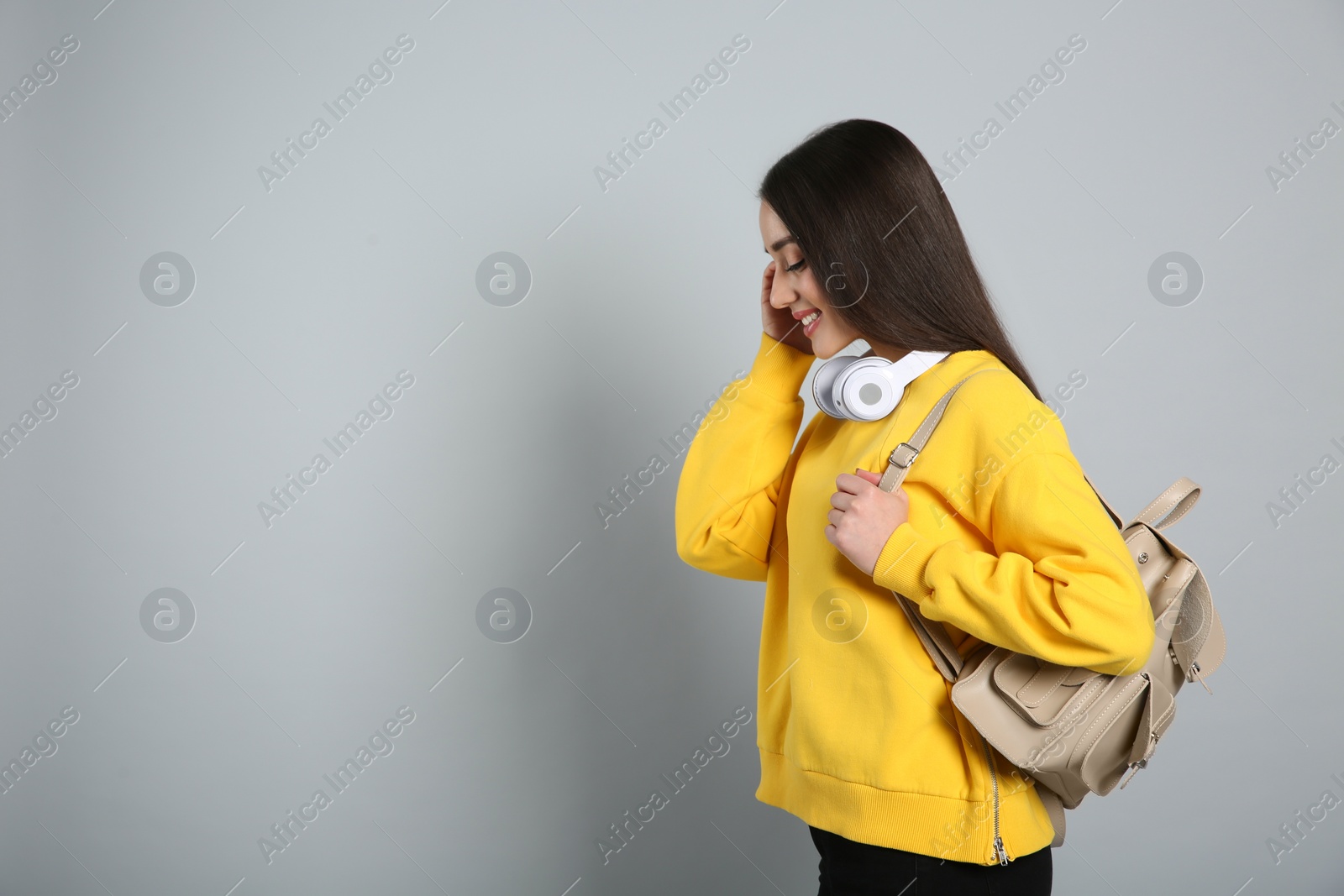 Photo of Beautiful young woman with stylish leather backpack and headphones on grey background. Space for text