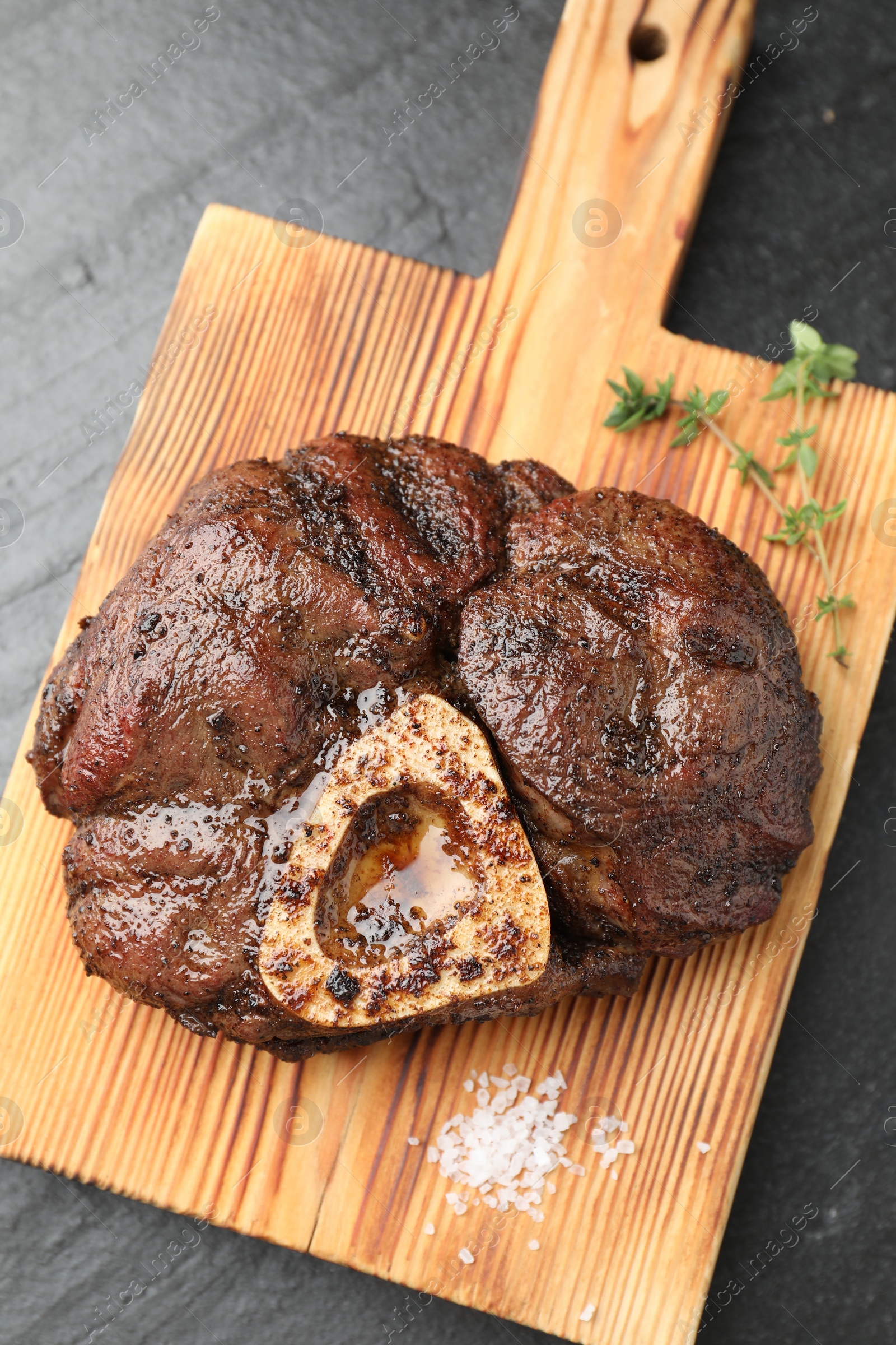 Photo of Piece of delicious grilled beef meat, thyme and salt on black table, top view