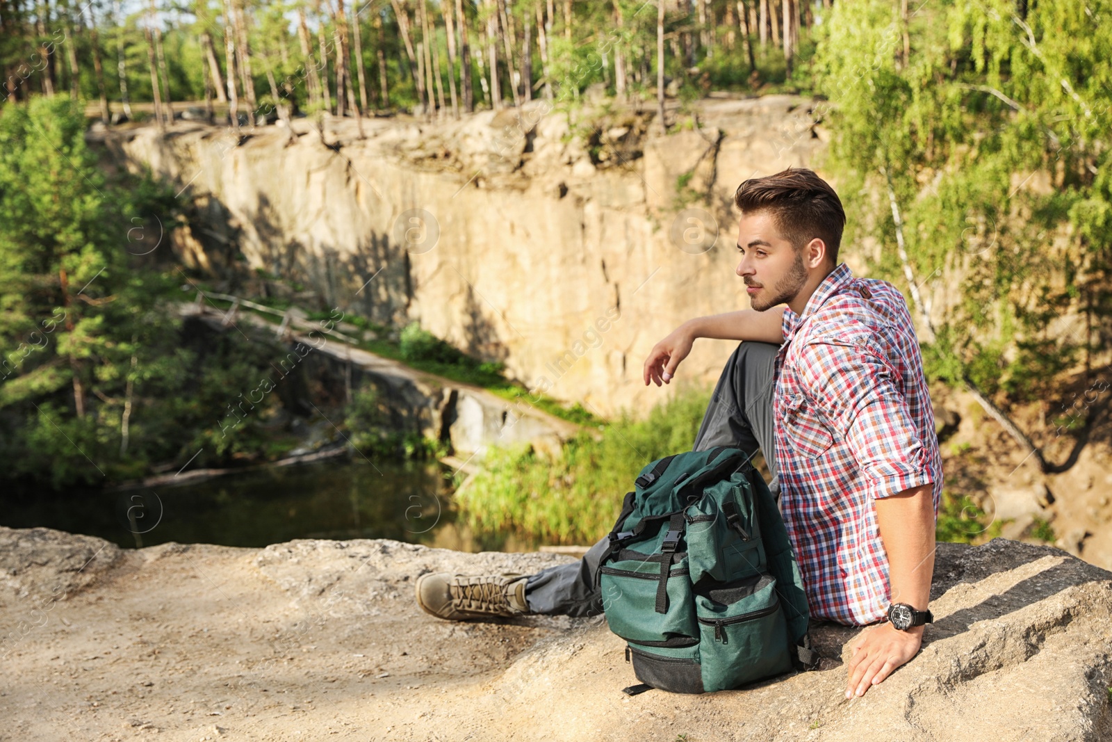 Photo of Young man on rock near lake and forest. Camping season