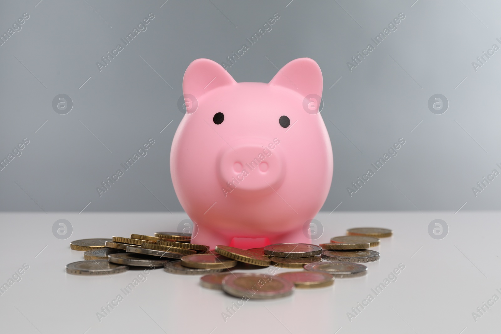 Photo of Pink piggy bank and coins on white table