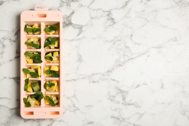 Ice cube tray with mint and lemon on marble background, top view. Space for text