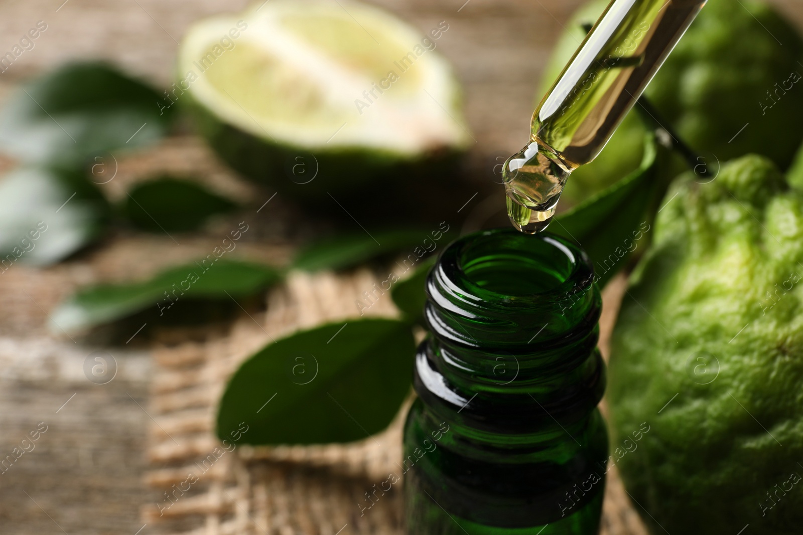 Photo of Bergamot essential oil dripping from pipette into bottle on table, closeup. Space for text