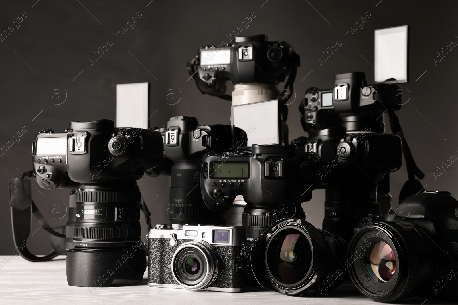 Photo of Modern cameras on white wooden table against dark background