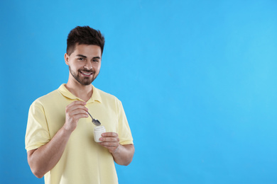 Photo of Happy young man with yogurt and spoon on light blue background. Space for text
