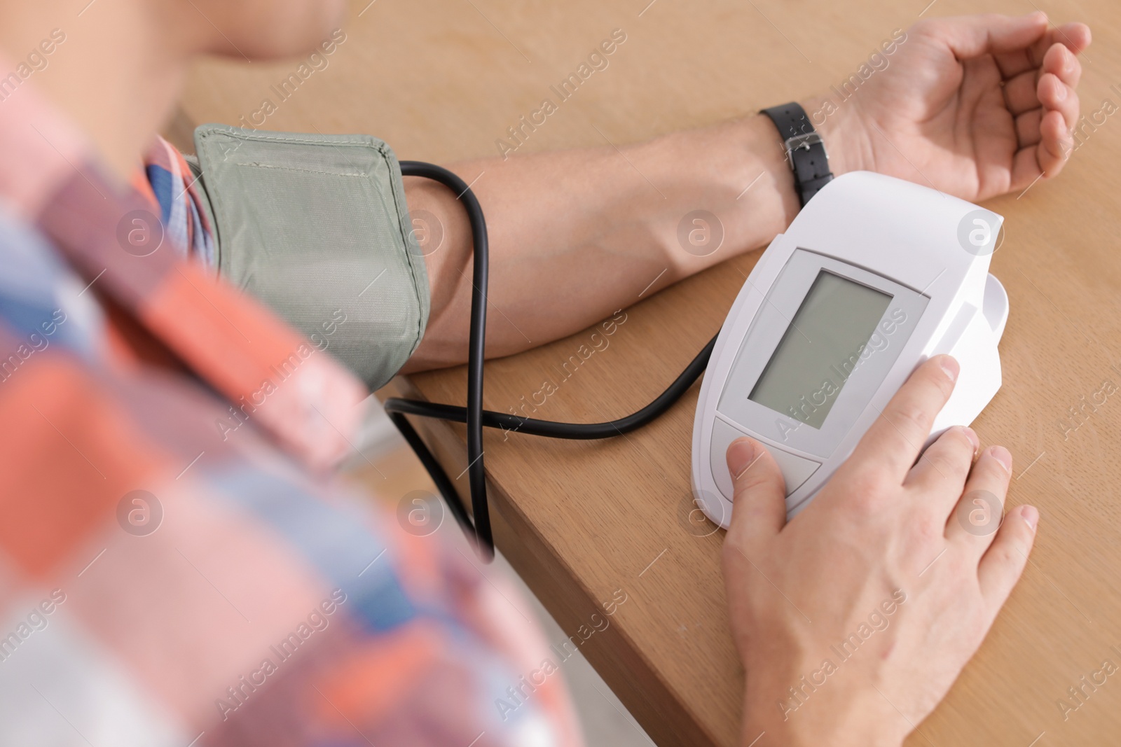 Photo of Man checking blood pressure with sphygmomanometer at table, closeup. Cardiology concept