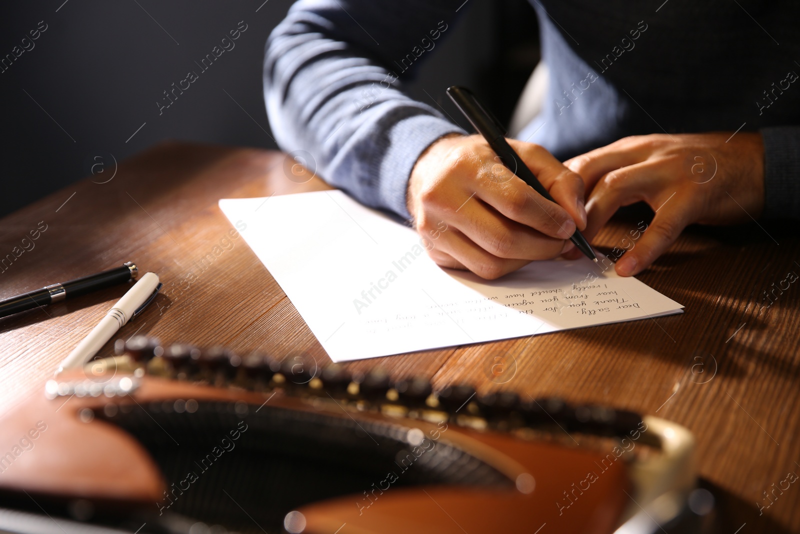 Photo of Man writing letter at wooden table indoors, closeup