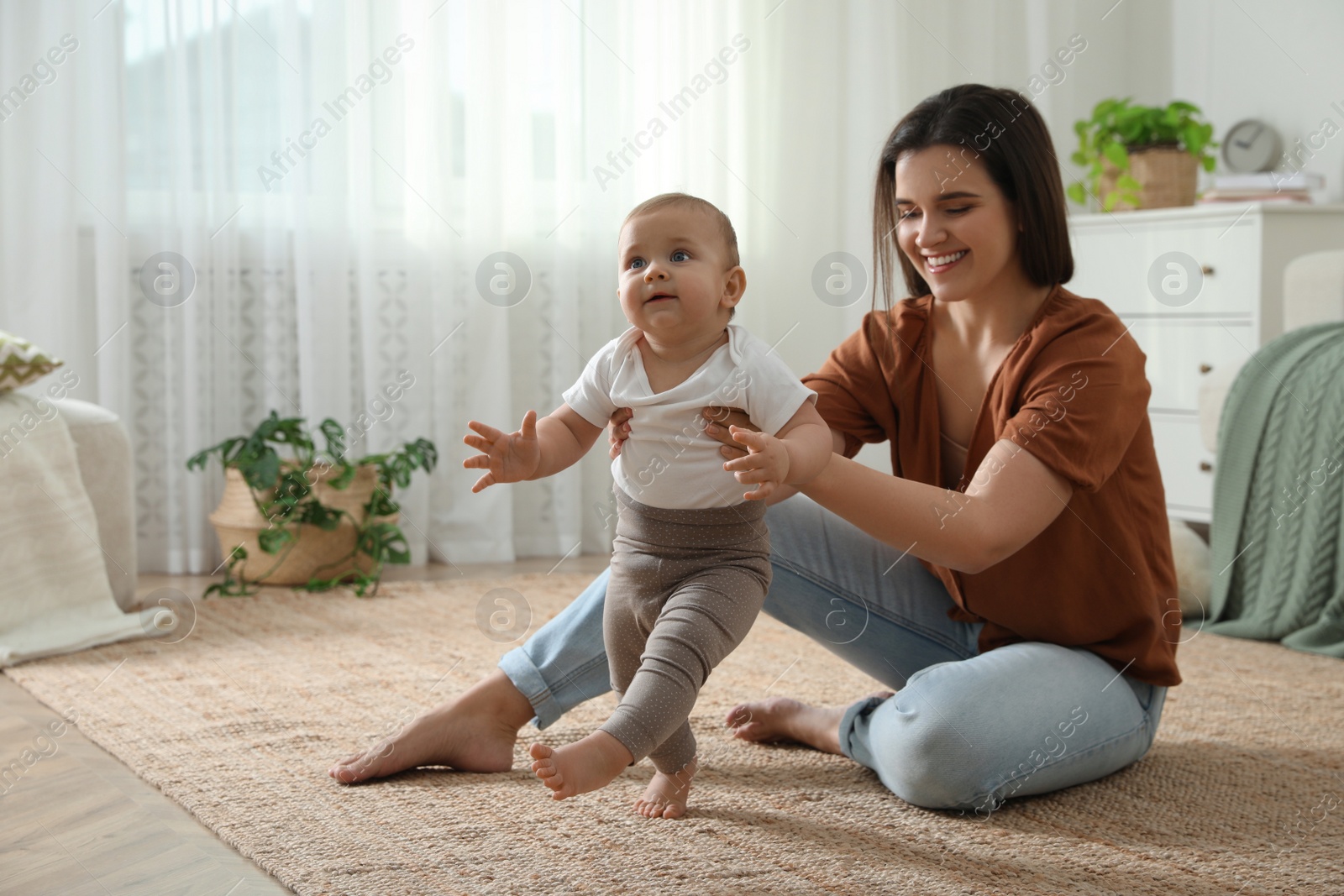 Photo of Mother supporting her baby daughter while she learning to walk at home