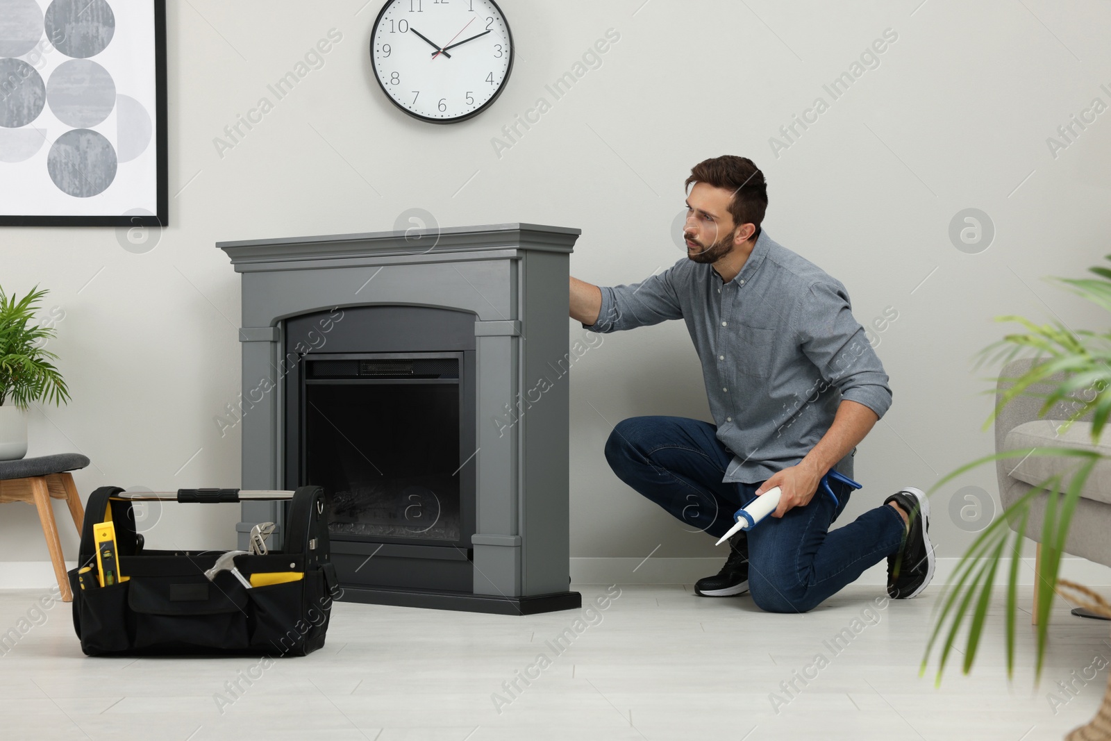 Photo of Man sealing electric fireplace with caulk near wall in room