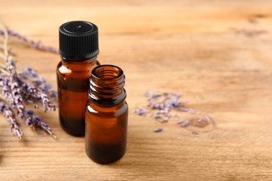 Essential oil and lavender flowers on wooden table, closeup. Space for text