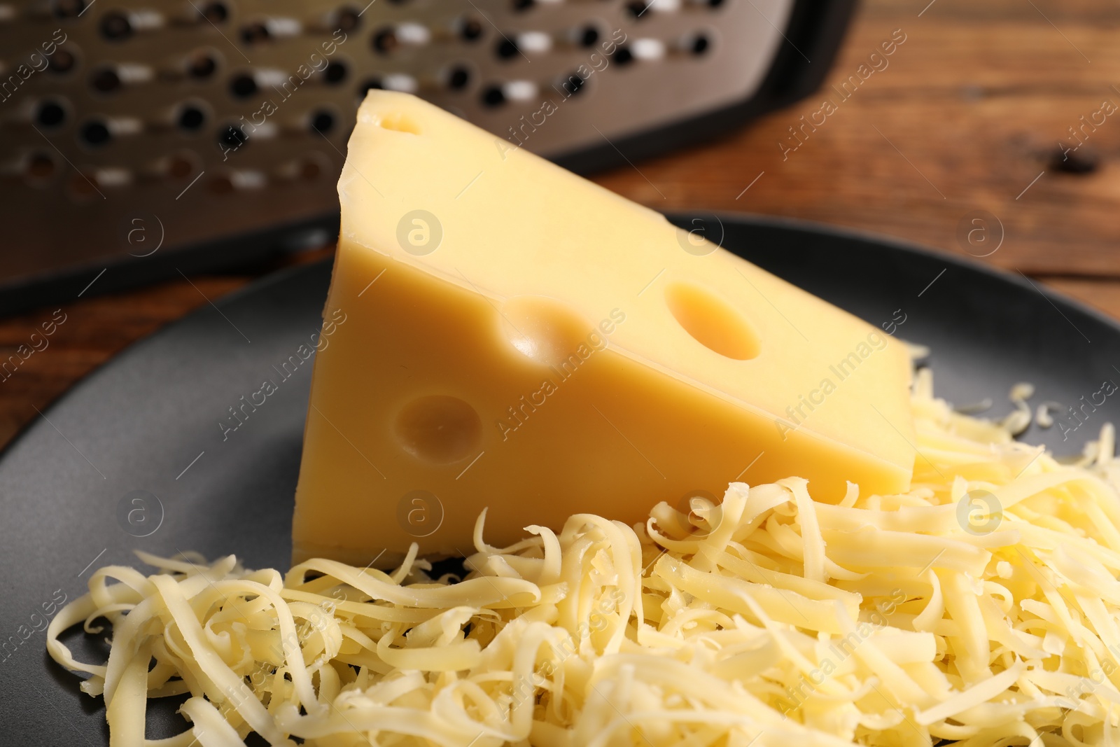 Photo of Grated and whole piece of cheese on wooden table, closeup