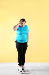 Photo of Overweight woman in sportswear using scales near color wall