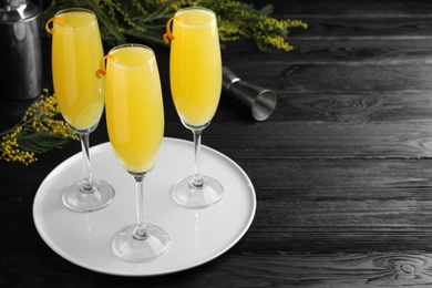 Photo of Glasses of Mimosa cocktail with garnish on dark wooden table. Space for text
