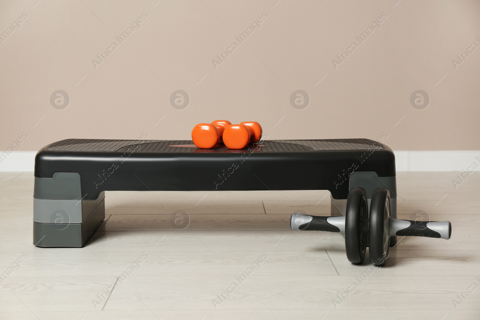 Photo of Step platform, dumbbells and abdominal wheel indoors. Sports equipment