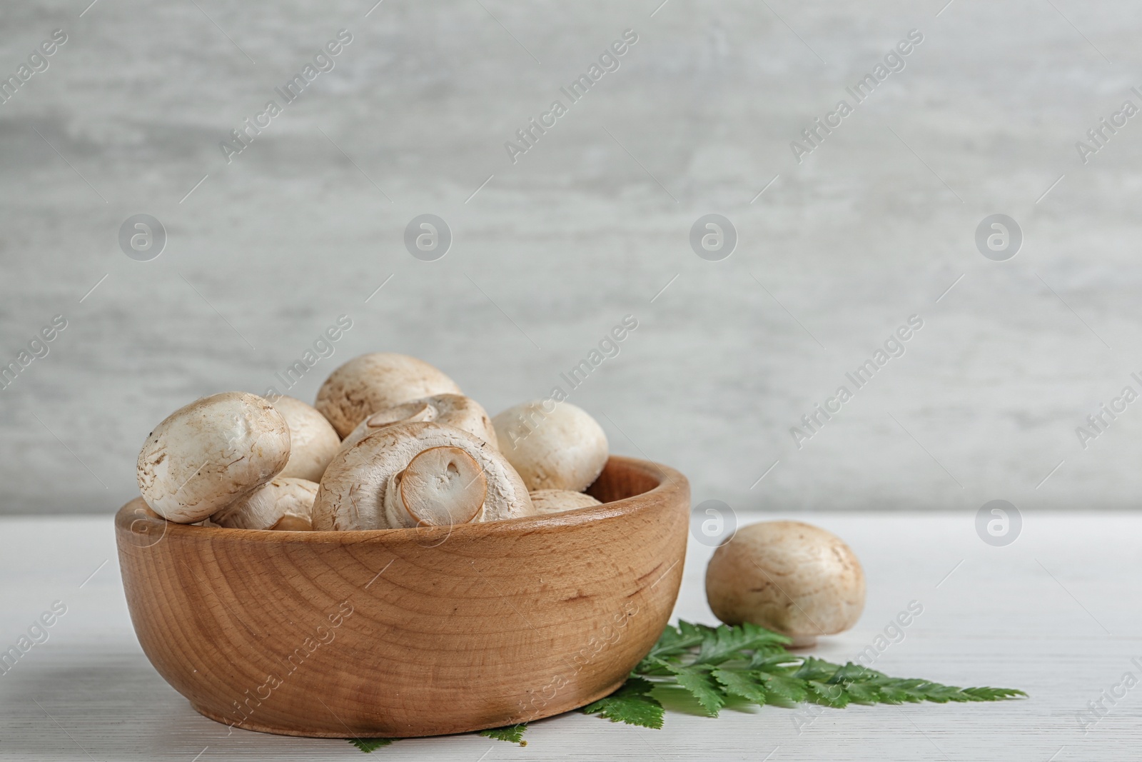 Photo of Bowl with fresh champignon mushrooms on wooden table, space for text