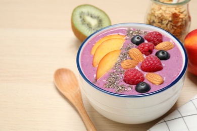 Photo of Delicious acai smoothie with fruits and almonds served on wooden table, closeup