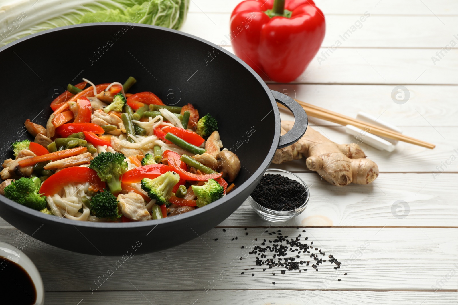 Photo of Stir fried noodles with mushrooms, chicken and vegetables in wok on white wooden table