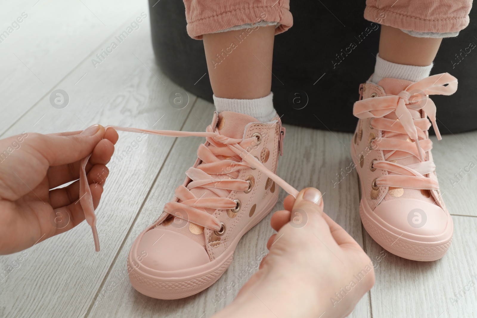 Photo of Mother helping daughter to tie shoe laces at home, closeup