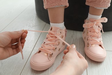 Photo of Mother helping daughter to tie shoe laces at home, closeup