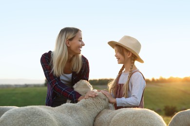 Photo of Mother and daughter stroking sheep on pasture. Farm animals
