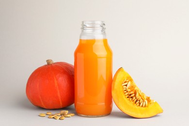 Photo of Tasty pumpkin juice in glass bottle, whole and cut pumpkins on light background