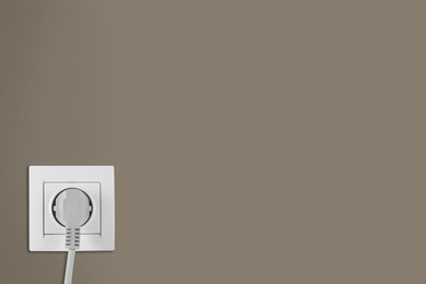 Image of Brown wall with power socket and inserted plug, space for text. Electrical supply