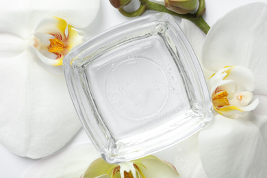 Photo of Bowl of cosmetic gel and beautiful flowers on white background, top view