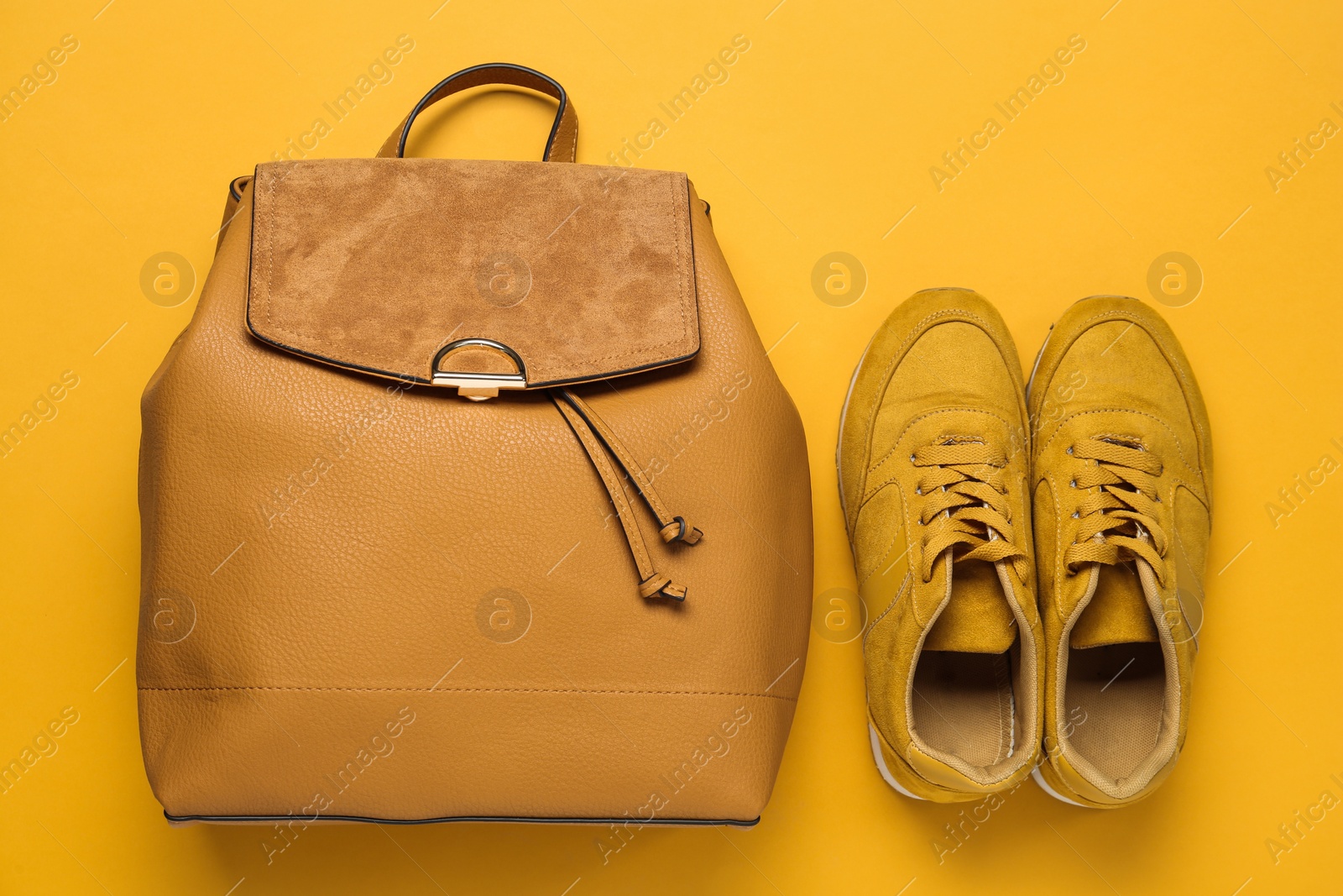 Photo of Stylish backpack and shoes on yellow background, flat lay