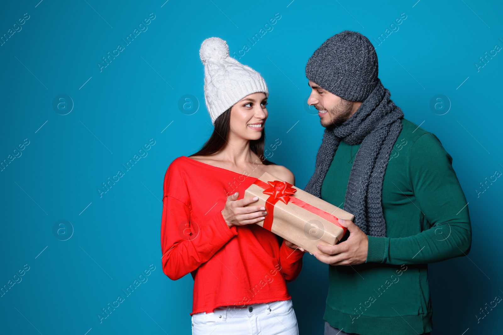 Photo of Young couple in warm clothes with Christmas gift on color background