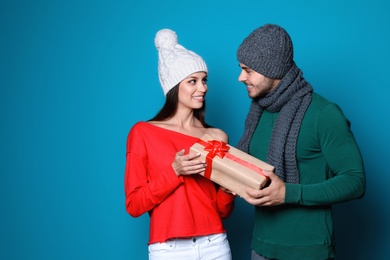 Young couple in warm clothes with Christmas gift on color background