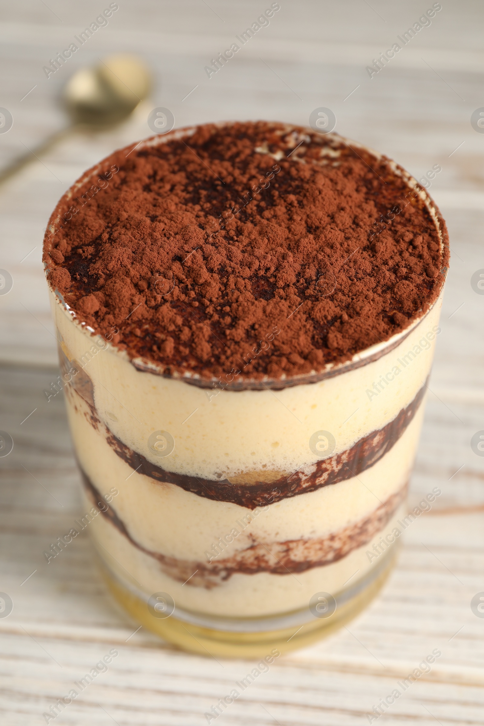 Photo of Delicious tiramisu in glass on light wooden table, closeup