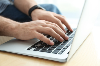 Photo of Man working on modern laptop at wooden table indoors, closeup