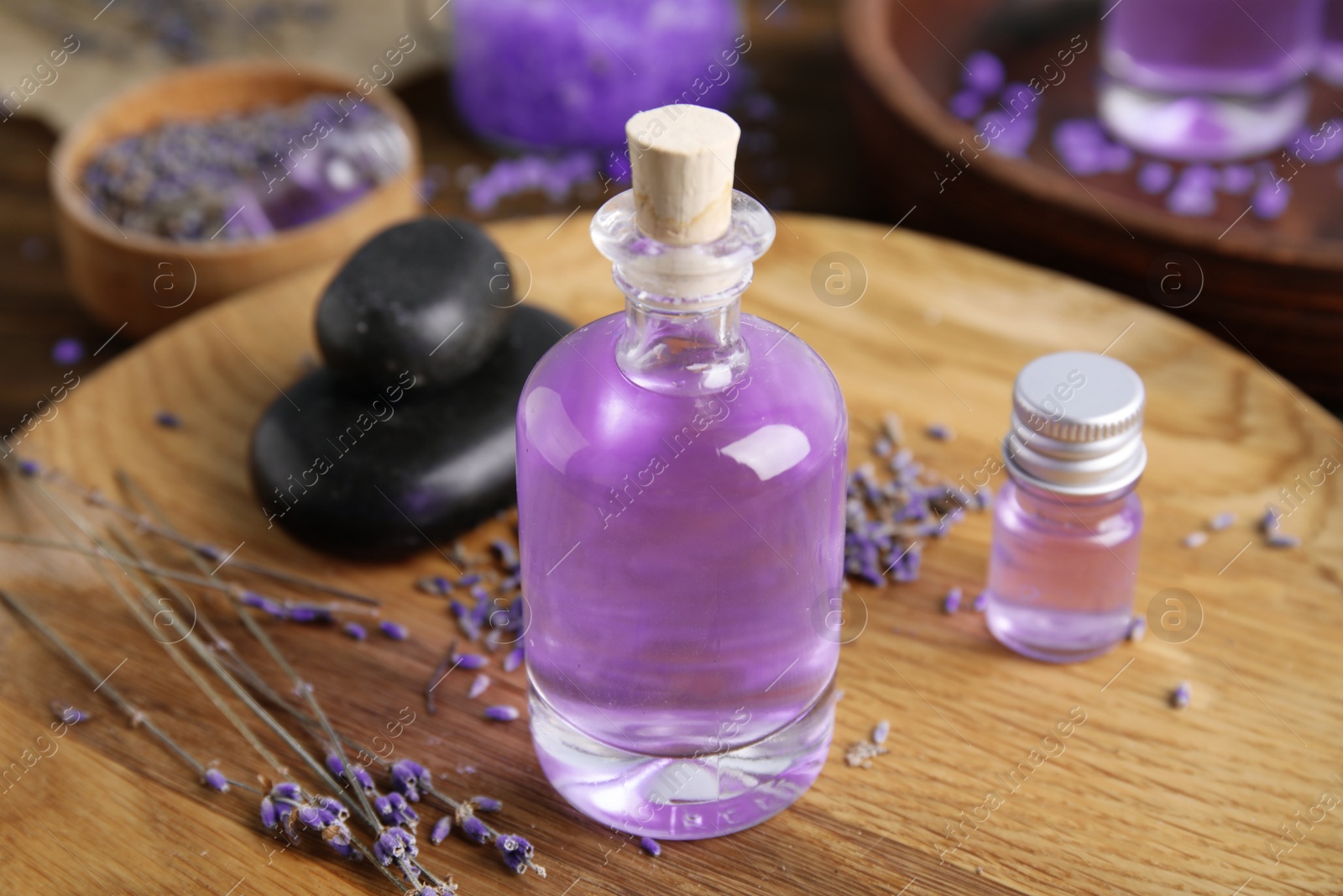 Photo of Natural herbal oil and lavender flowers on wooden plate, closeup