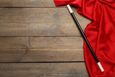 Photo of Beautiful black magic wand and red fabric on wooden table, top view. Space for text