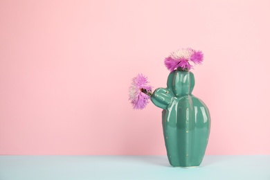 Photo of Trendy cactus shaped ceramic vase with flowers on table against color background