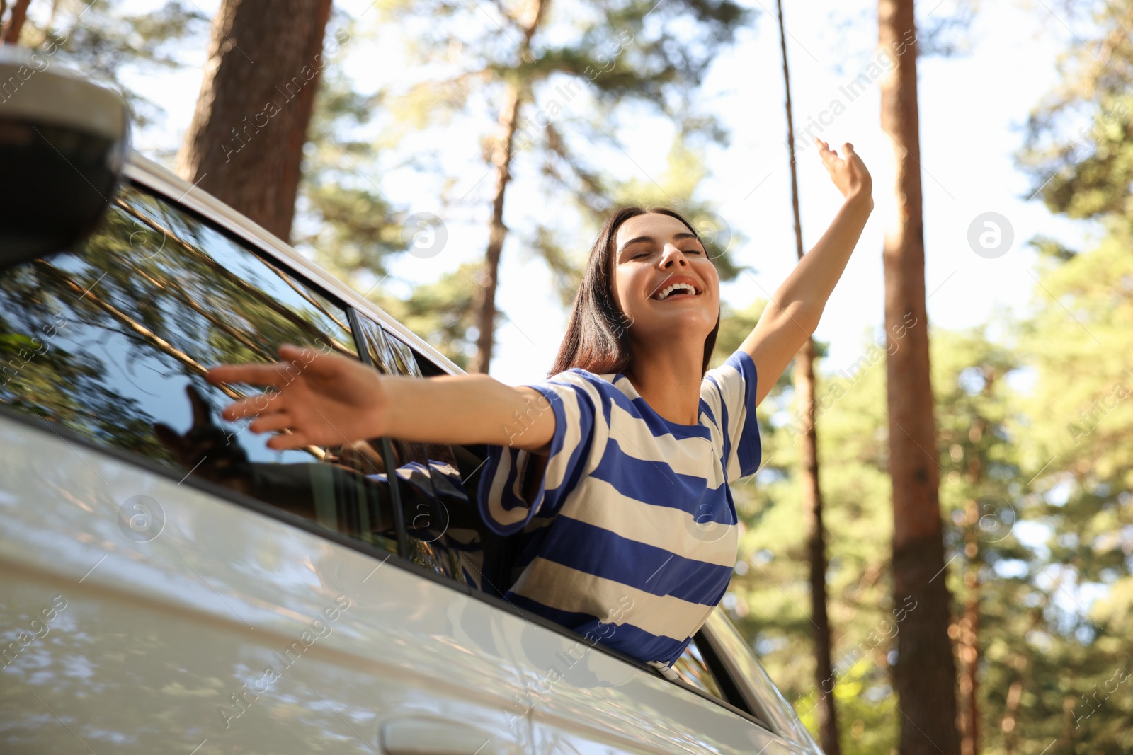 Photo of Enjoying trip. Happy young woman leaning out of car window, low angle view
