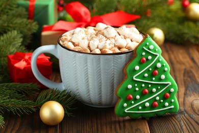 Photo of Tasty Christmas cookie in shape of fir tree, cocoa with marshmallows and festive decor on wooden table, closeup