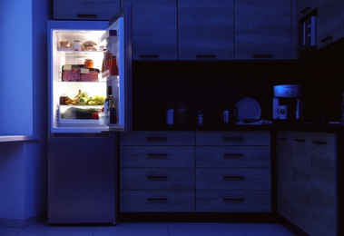 Photo of Open refrigerator full of products in kitchen at night