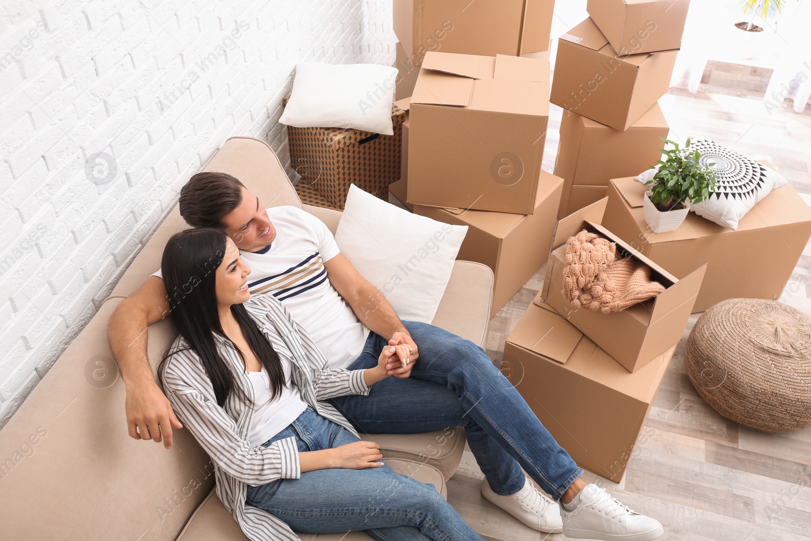 Photo of Happy couple resting in room with cardboard boxes on moving day, above view